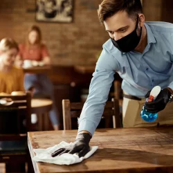 young-waiter-wearing-protective-face-mask-while-cleaning-tables-while-working-cafe